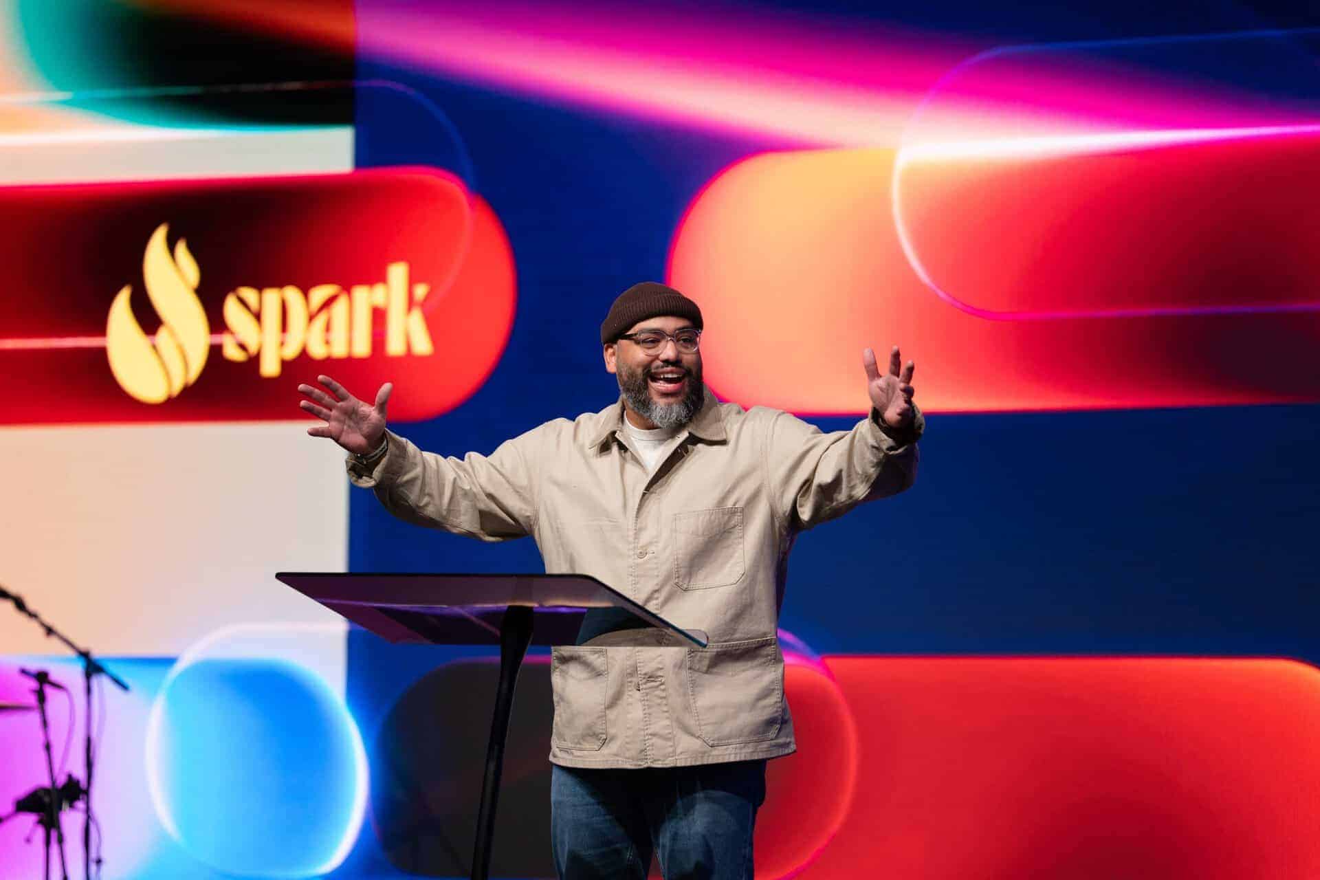 A speaker at the Katoomba Christian Convention Spark event delivering a presentation on stage with vibrant background visuals.