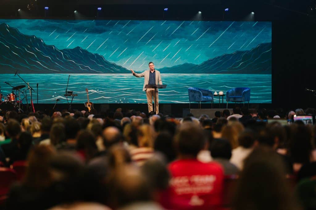 Speaker on stage at Katoomba Christian Convention during 'Fear Not' event, with a large audience and scenic mountain backdrop on screen.
