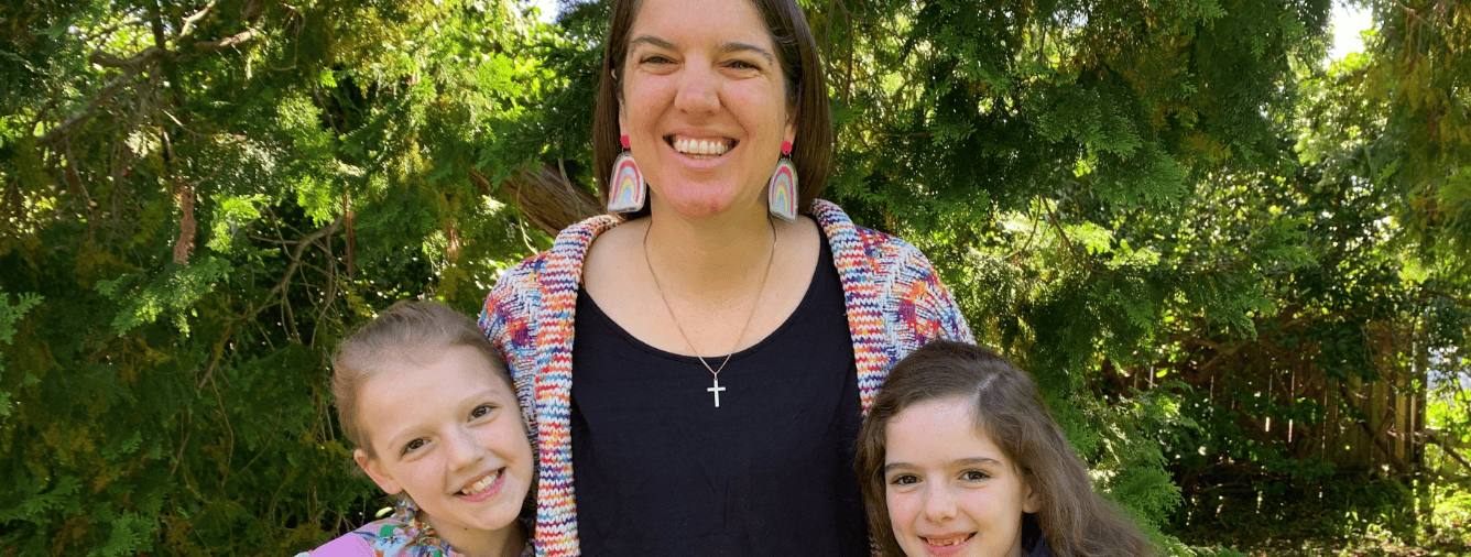 Anna smiling with two young girls outdoors in a garden setting, discussing motherhood and raising tweens.