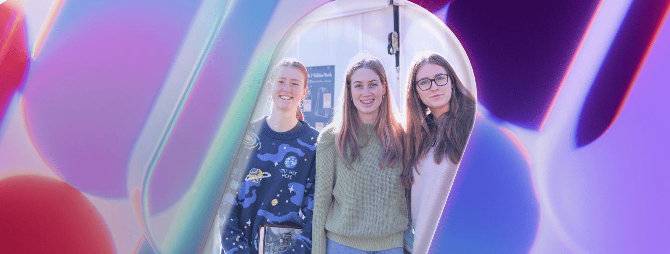 Three young women smiling at the Katoomba Christian Convention during a vibrant, colorful event related to Spark 2026 preparations.