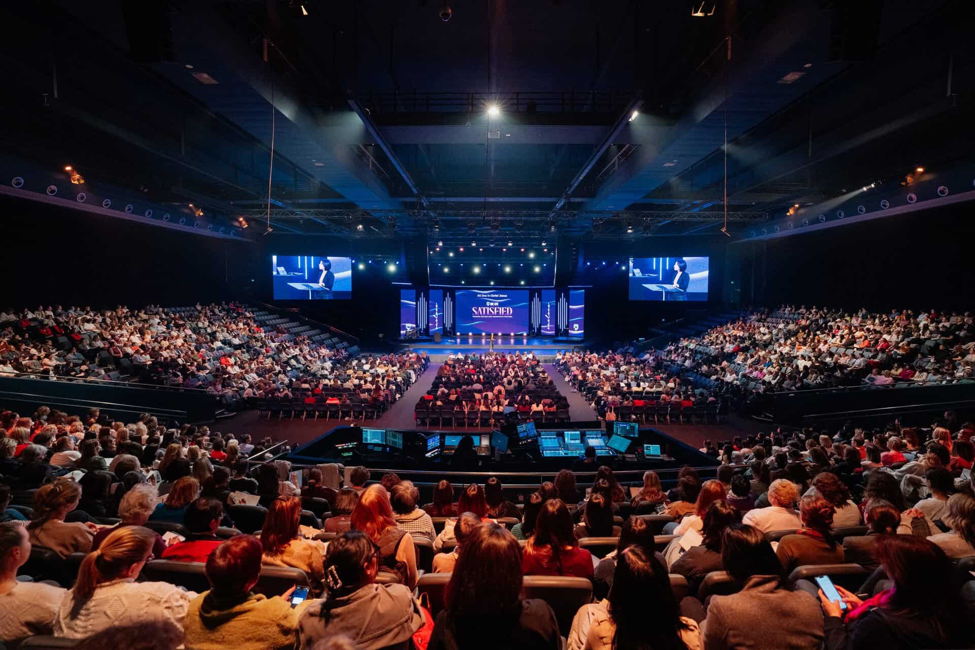 Large audience attending a Christian conference at Katoomba Christian Convention with stage and screens displaying speakers.