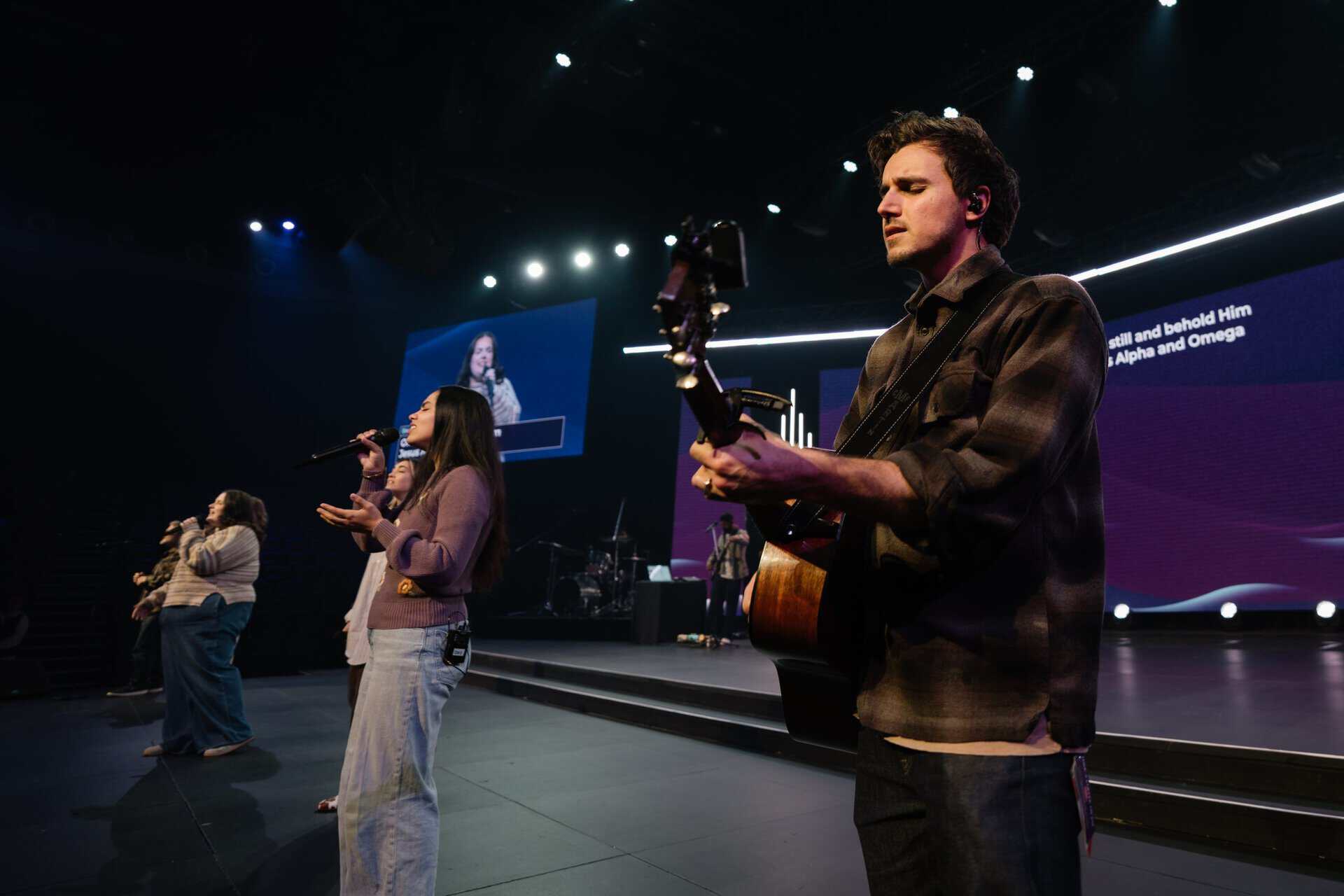 Young musicians and singers performing on stage at Katoomba Christian Convention, with a large screen displaying lyrics in the background.