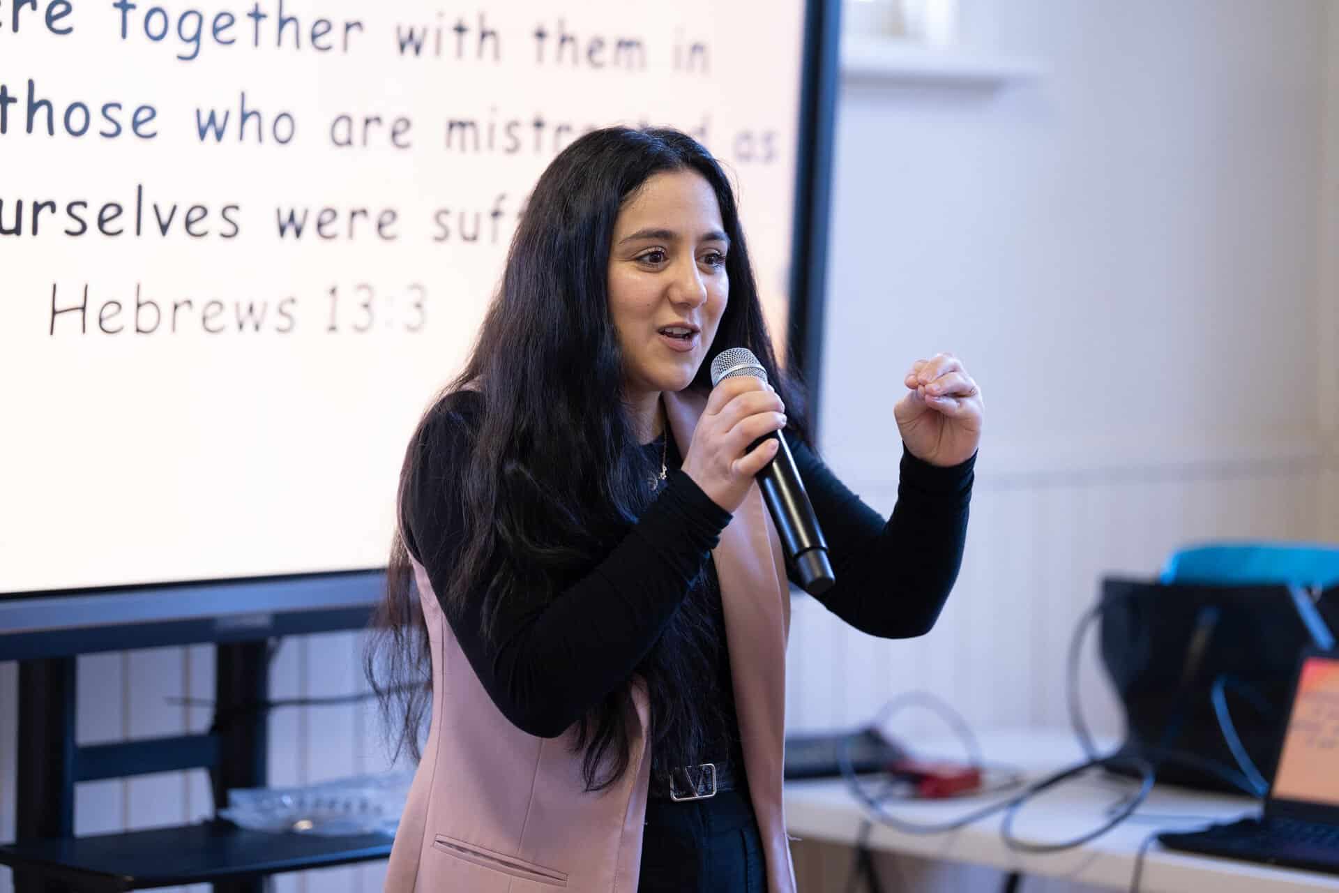 Young woman speaking into a microphone during a conference at Katoomba Christian Convention, with a presentation slide in the background.