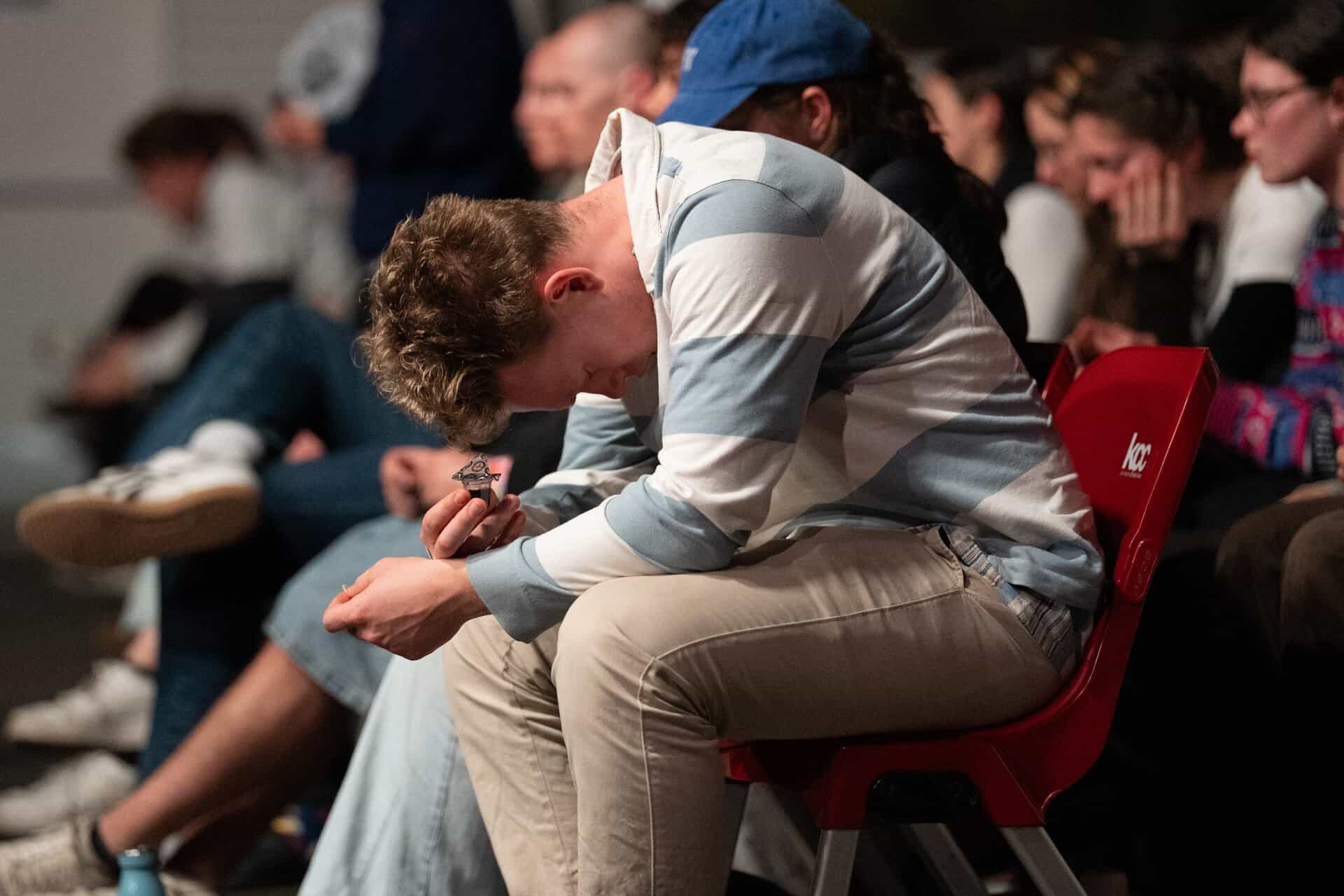 Young man with curly hair praying with head bowed and eyes closed during a Christian event at KCC in Katoomba.